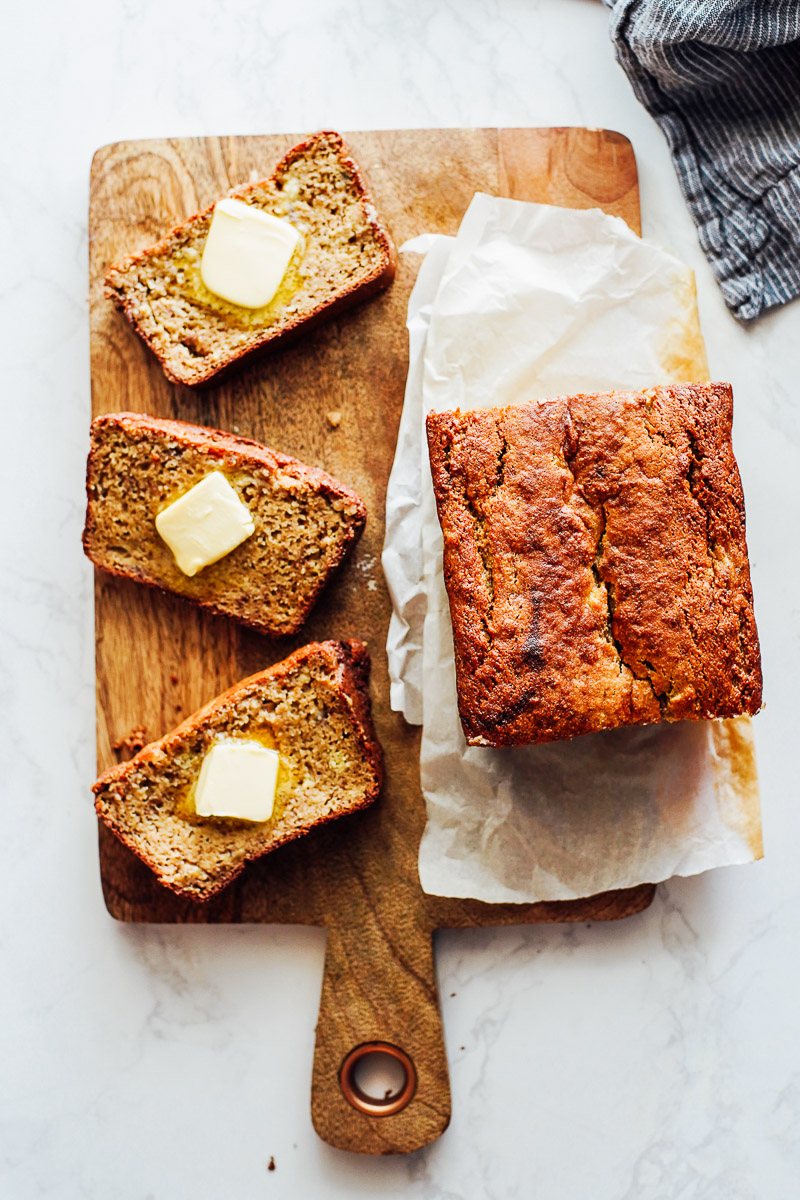 Banana bread sliced on a cutting board with butter on top of each slice.