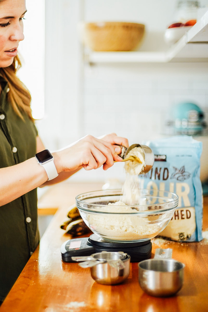 Adding almond flour to a large glass bowl, using a scale to weigh the flour.