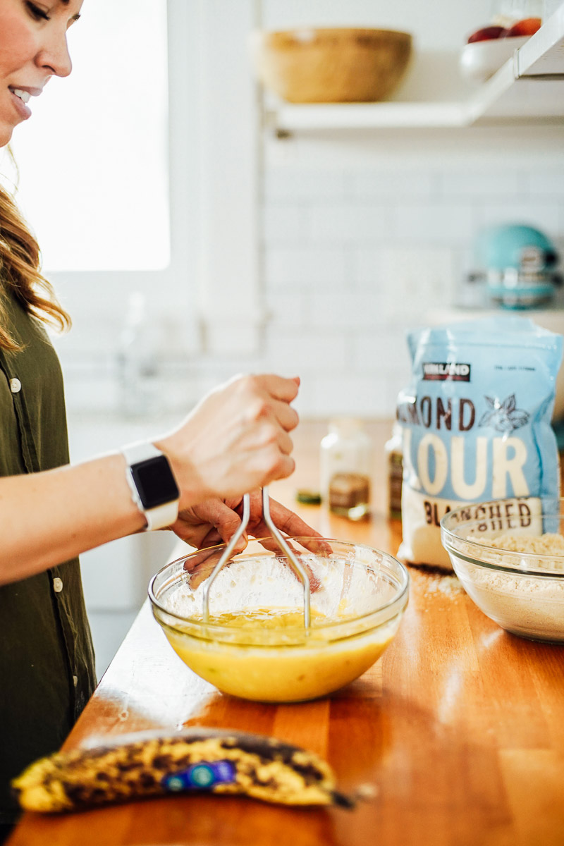 Mashing bananas in a glass bowl using a potato masher.