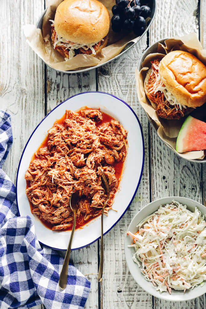 BBQ pulled chicken on a serving patter with coleslaw and buns on the side.