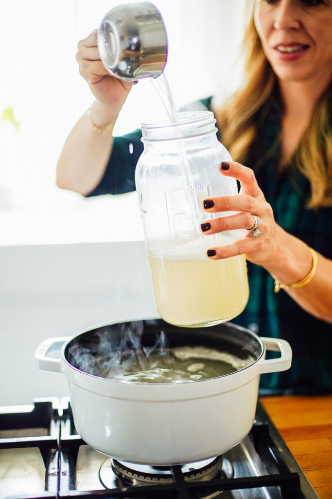 Making homemade laundry soap, spooning the soap into a glass jar from a cooking pot.