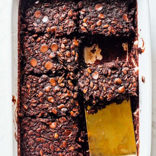 Baked chocolate oats in a pan, a gold spatula removing a slice.