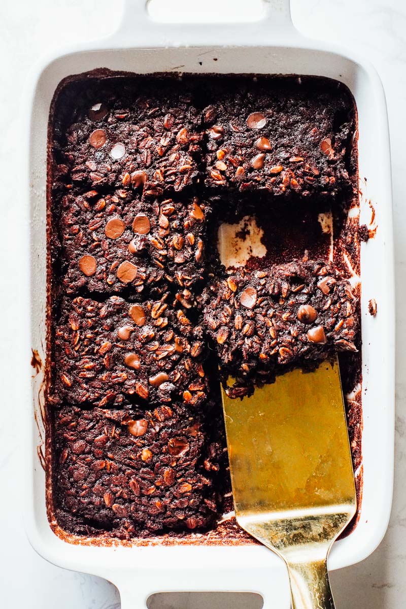 Baked chocolate oats in a pan, a gold spatula removing a slice.