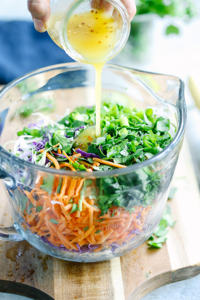 Pouring dressing over the top of the coleslaw. 