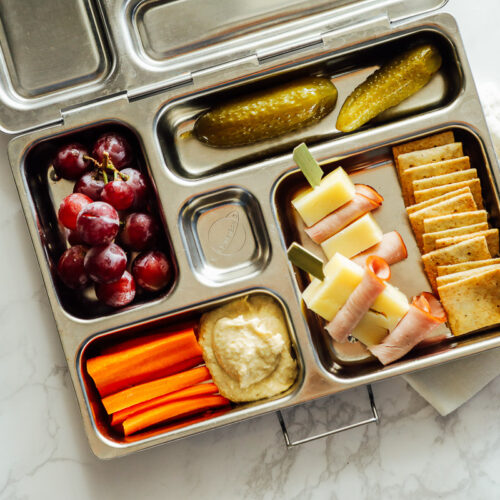 Homemade cheese, crackers, and ham lunchable with carrots, hummus, grapes, and a pickle.