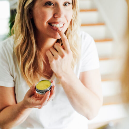 Applying lip balm from a metal tin to lips.