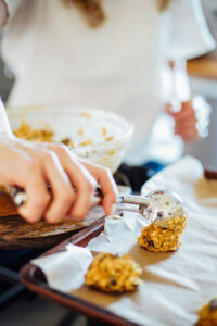 Using an ice cream scooper to scoop the cookie dough from the bowl to a sheet pan.