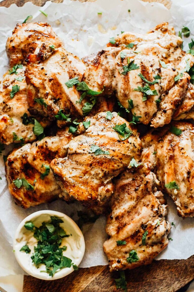 Grilled boneless chicken thighs, cooked, on a cutting board ready to be served.