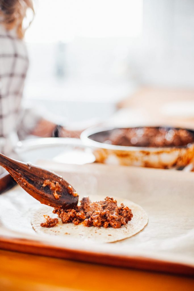 spooning ground beef mixture into tortillas