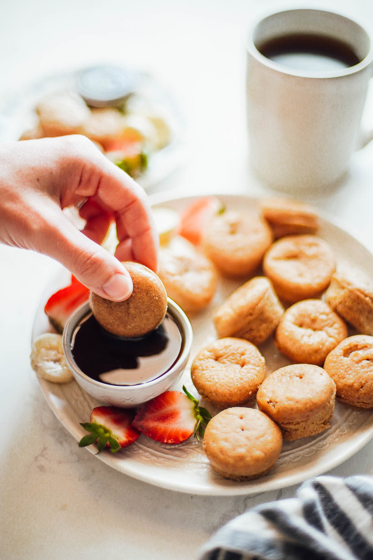 Mini pancakes on a plate, with hand dipping a pancake into maple syrup.