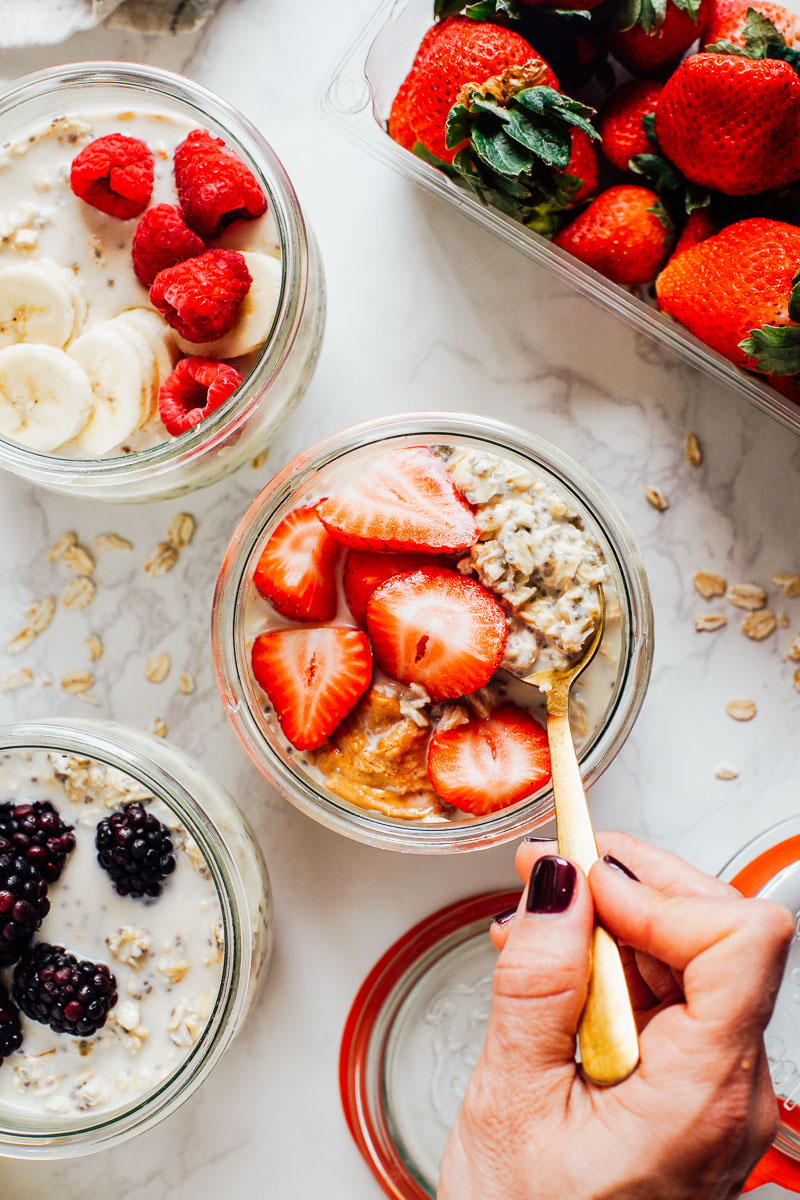 Spooning overnight oats from a glass bowl, with strawberries on top.