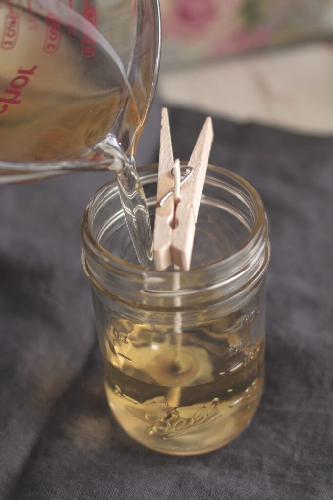 Pouring melted wax into a mason jar with a wick. 