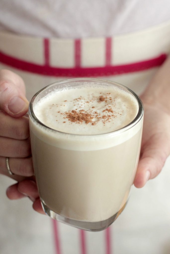 Hands holding a chai tea latter in a glass mug.