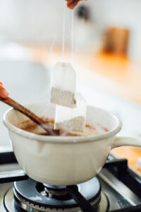 Adding tea bags to a pot of chai spices and water on the stove-top.