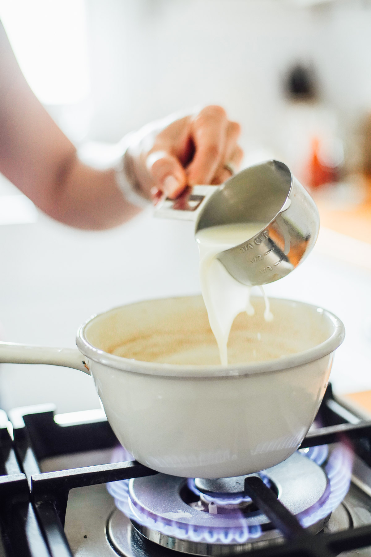 Pouring milk into a white pot on the stove-top.