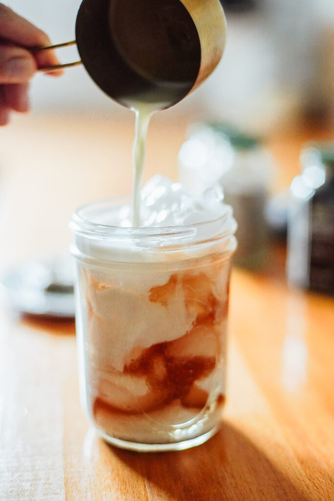 Pouring milk into a glass with ice and chai concentrate.