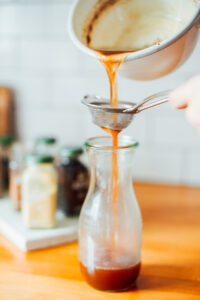 Staining the chai tea concentrate through a fine mesh strainer into a glass bottle.