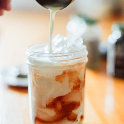 Pouring milk into a mason jar filled with ice and chai concentrate.