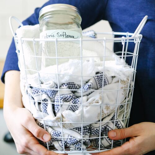 Holding a laundry basket with towels and liquid laundry fabric softener inside.