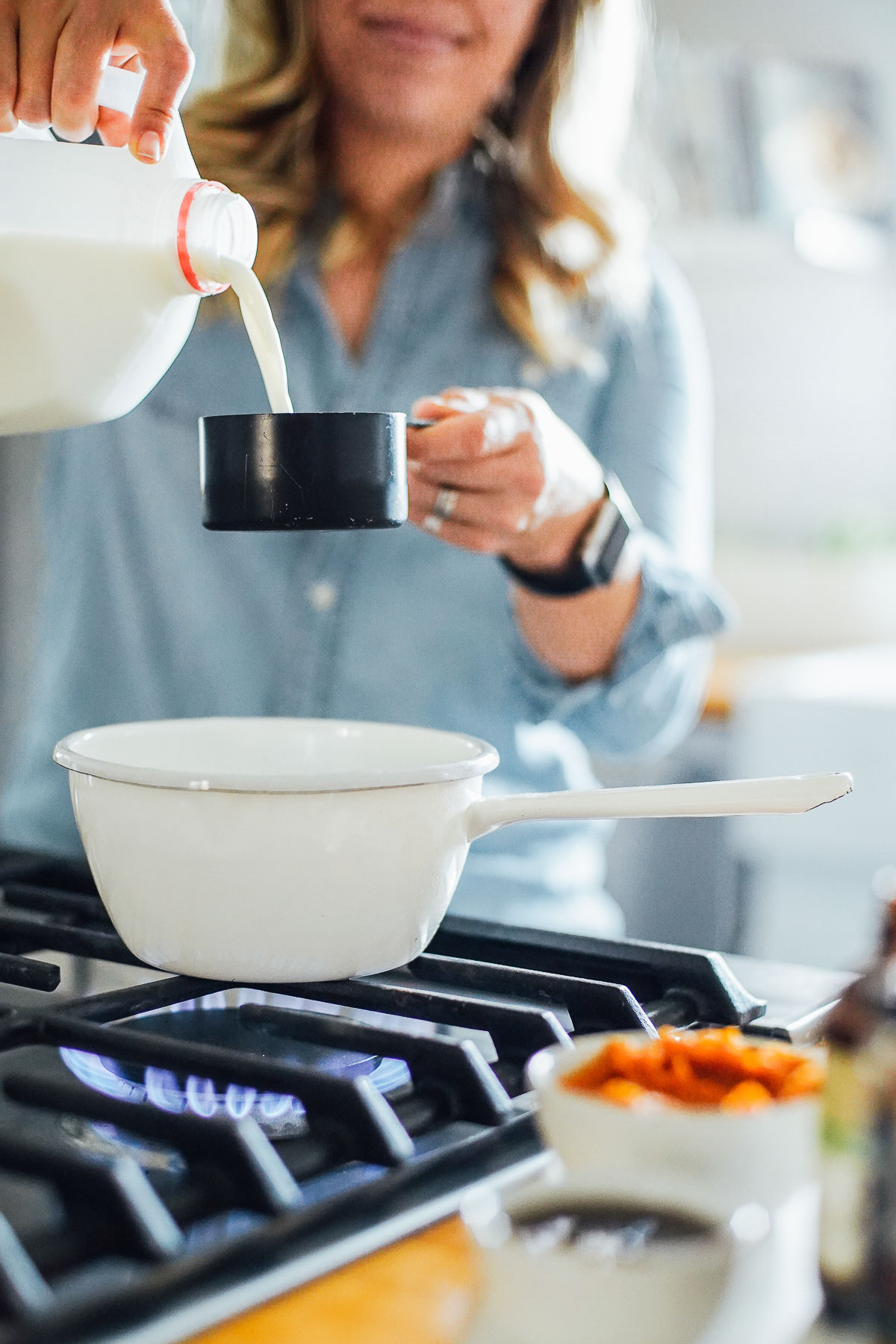 Adding milk to a black measuring cup over a white saucepan.