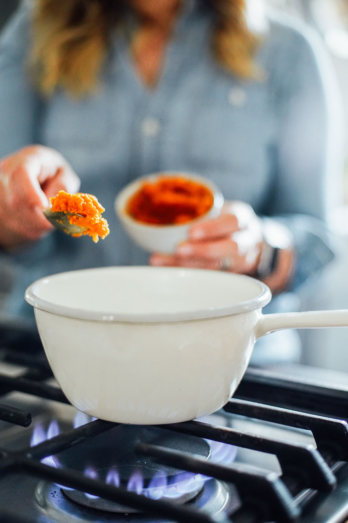 Adding pumpkin puree to a white saucepan on a stove-top.