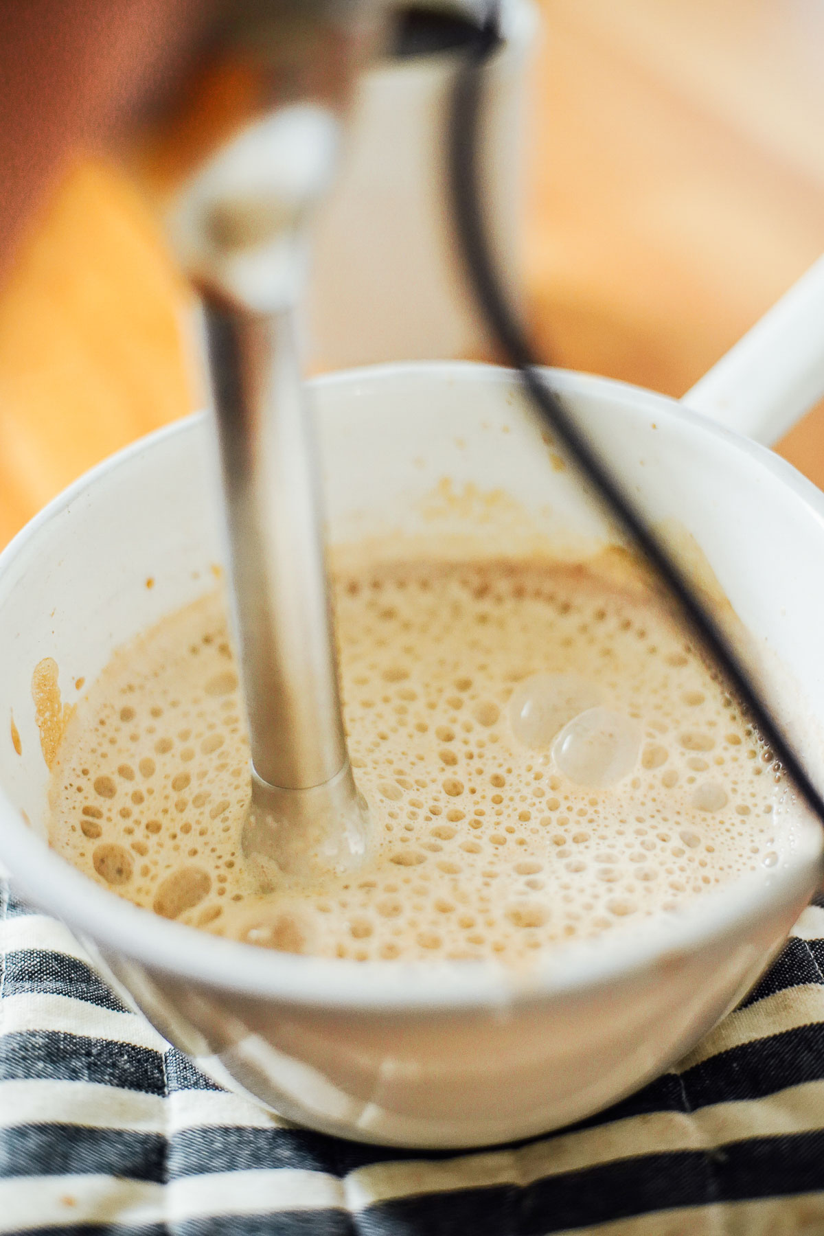 Using an immersion blender to blend milk and pumpkin puree in a white saucepan.