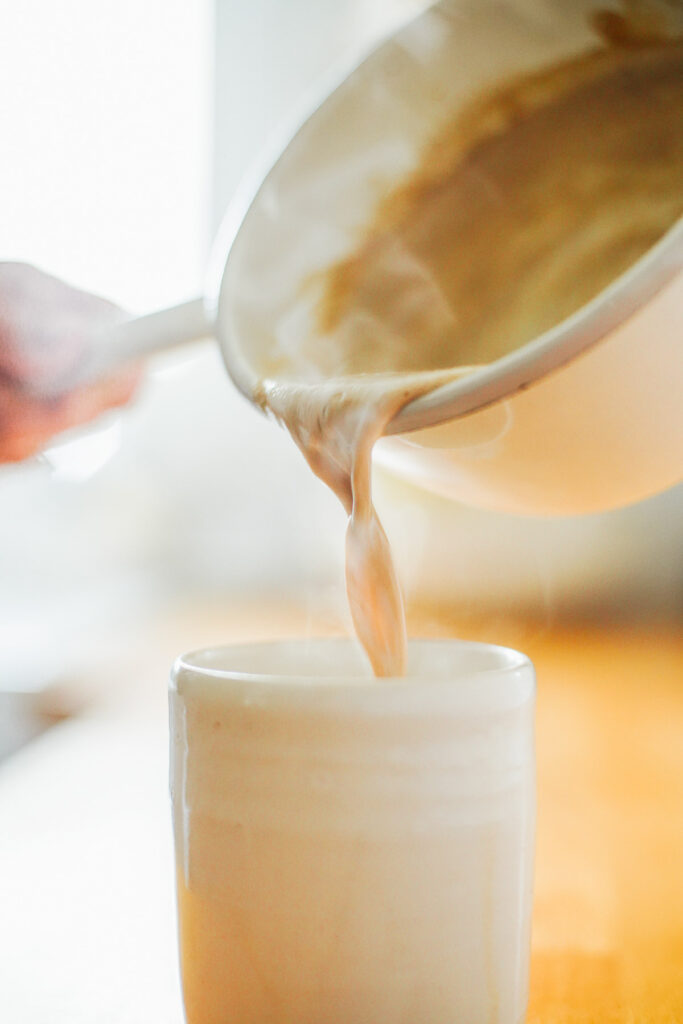 Pouring hot milk from a saucepan into a mug.