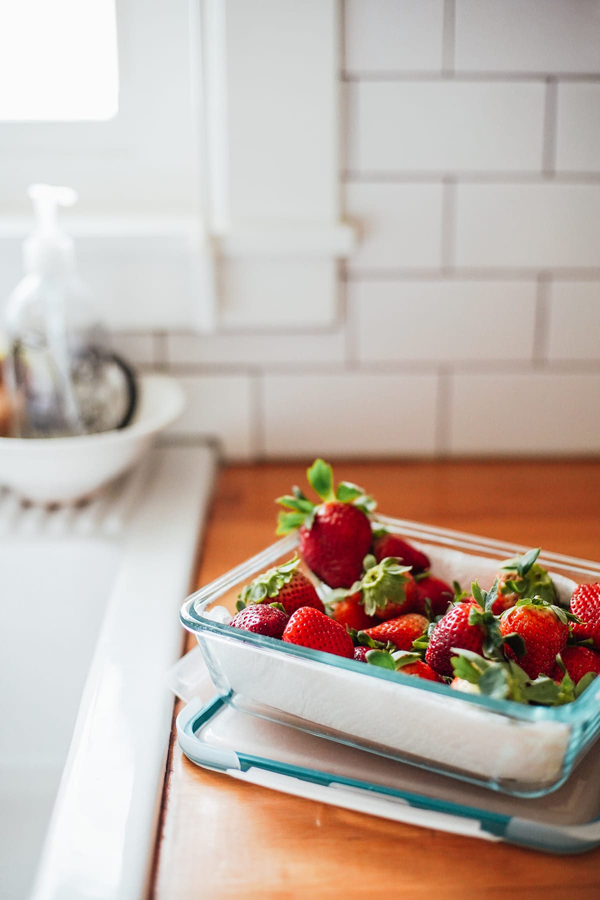 Strawberries in a glass jar lined with a paper towel on the kitchen counter.