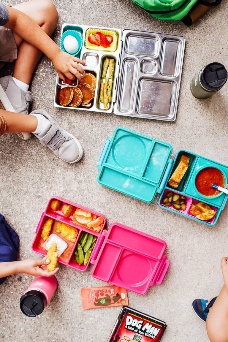 3 lunchboxes on the ground: with chicken nuggets, with soup, and with pancakes.