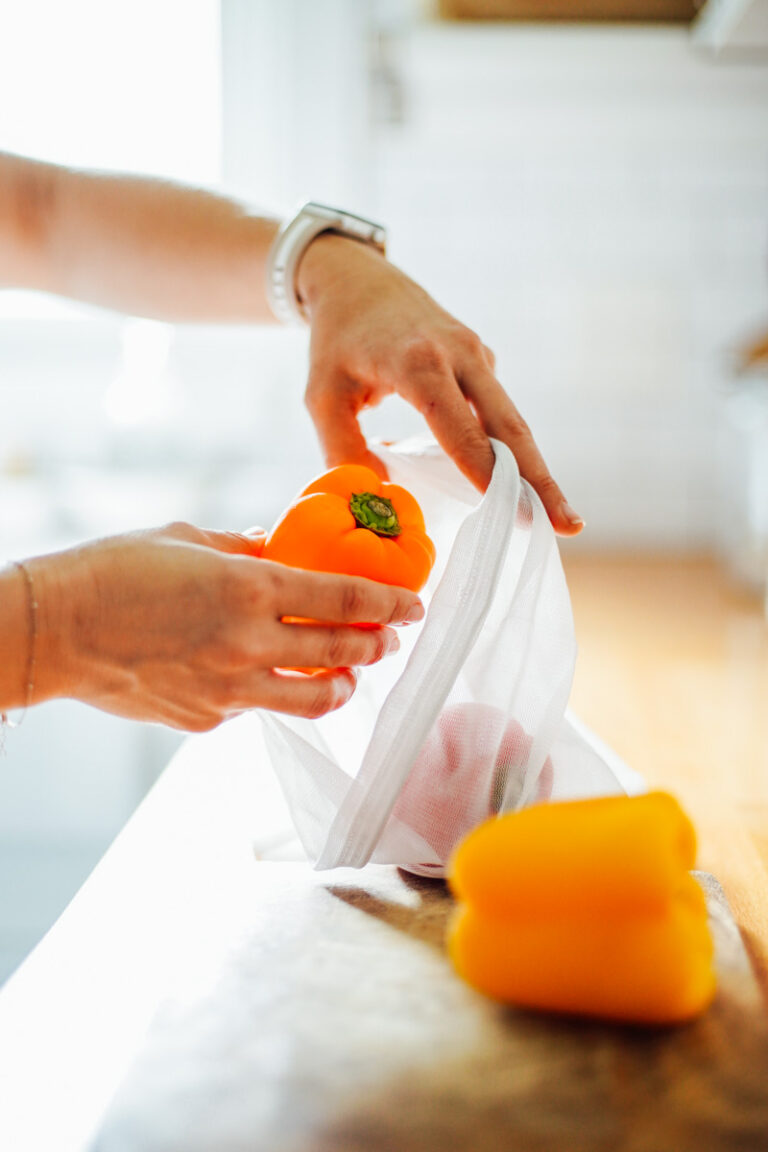 Placing an orange bell pepper in a reusable bag.