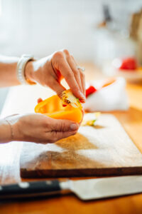 Halved yellow bell pepper with the seed being removed by a hand.