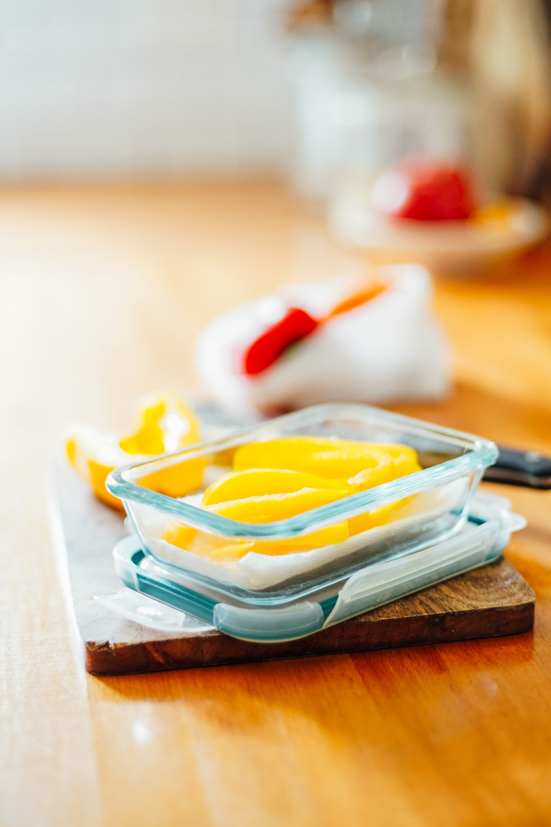 Sliced yellow bell pepper sticks in an airtight container lined with a paper towel. 