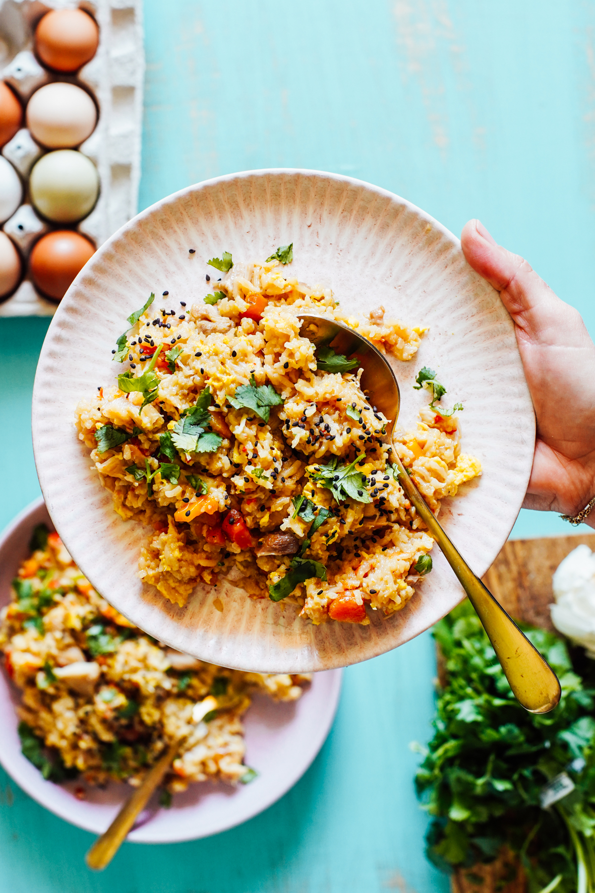 Hand holding a pink plate with a pile of fried rice and a gold spoon.