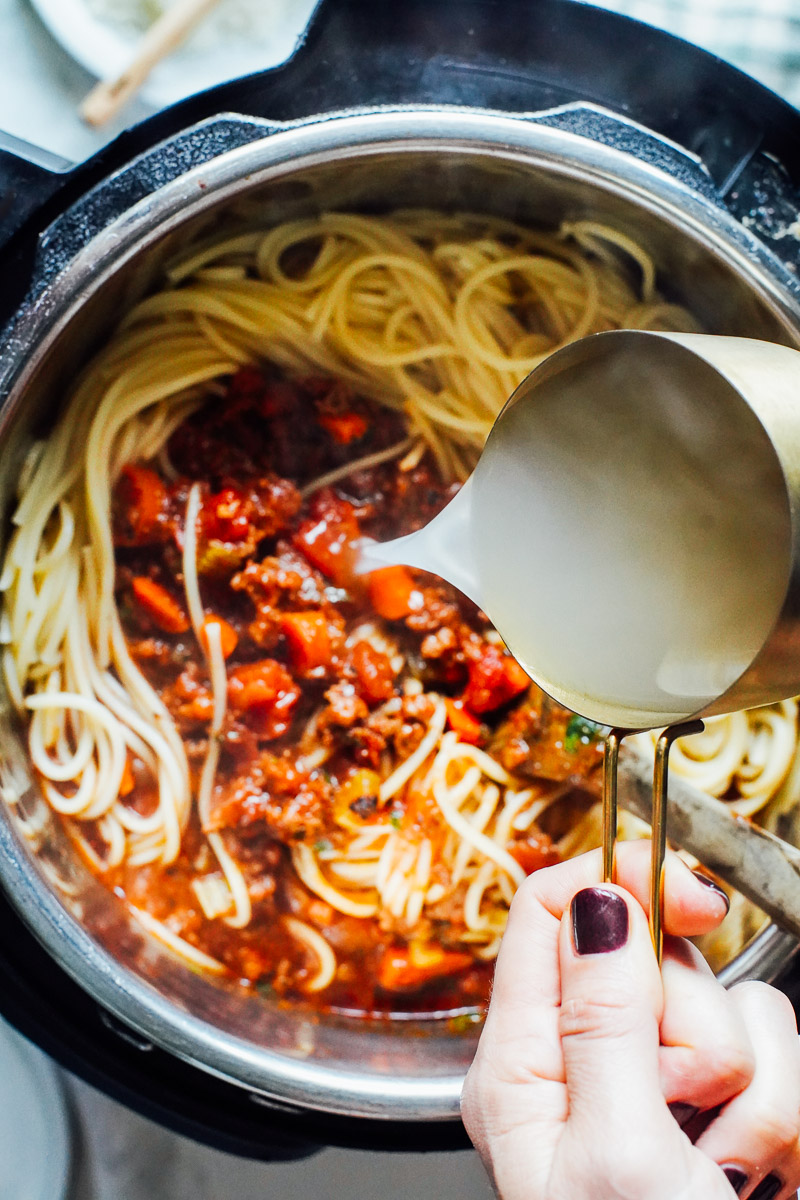 Pouring pasta water into the pasta mixed with bolognese sauce.