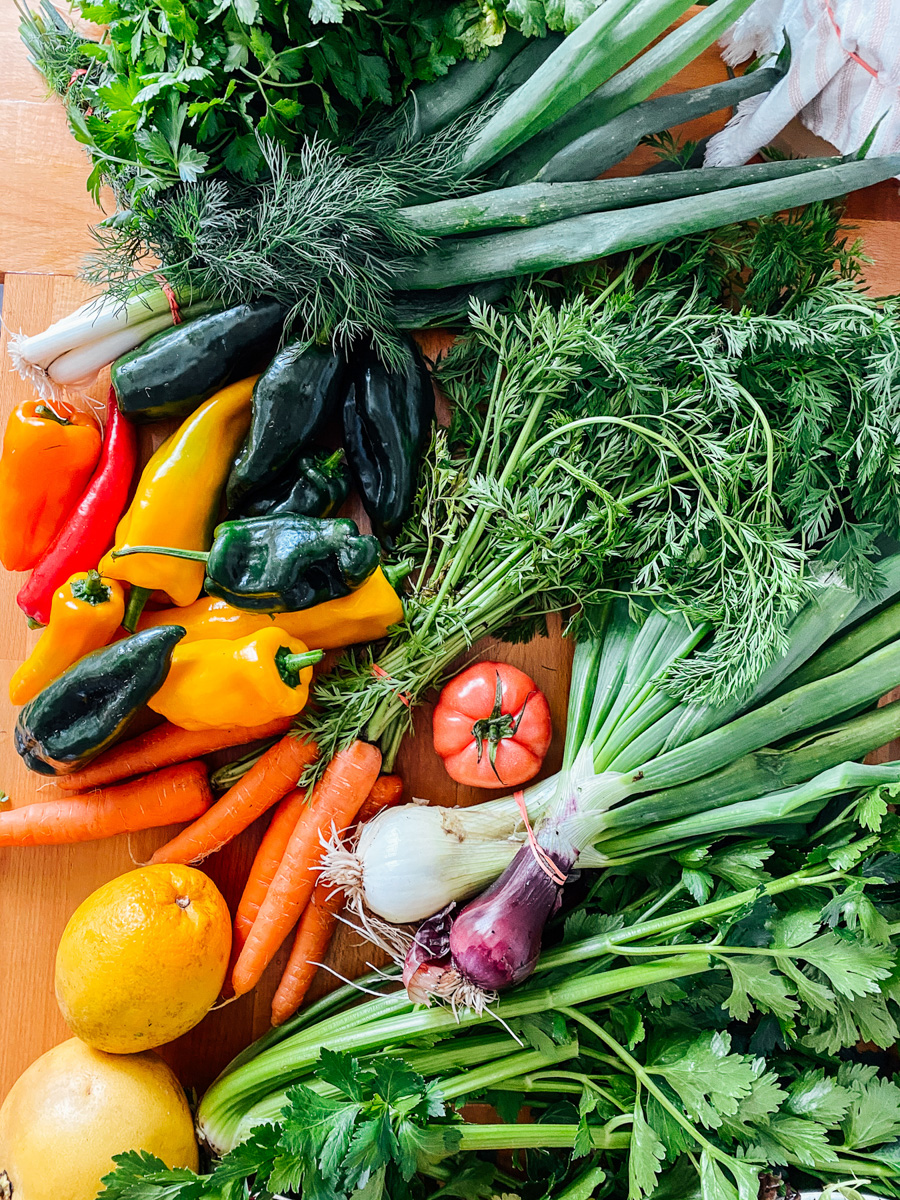 Farmer's market produce with bell peppers in the mix: carrots, onions, yellow peppers, green onions.