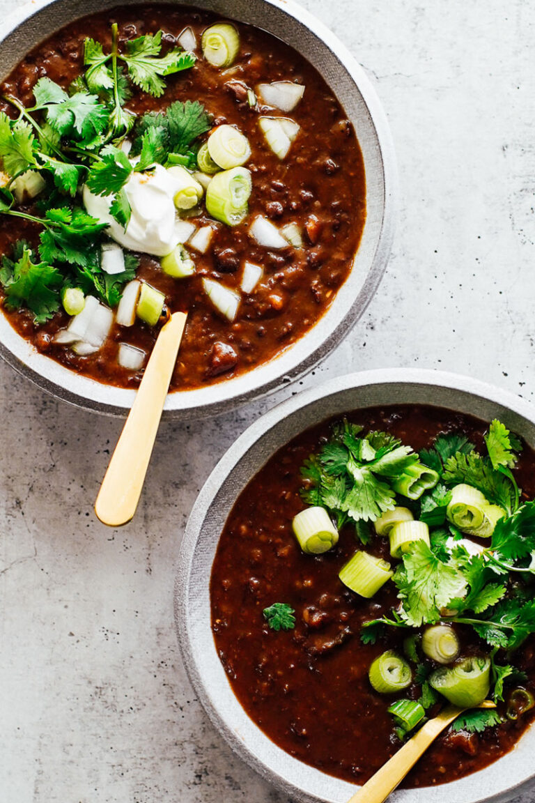 Black bean soup in bowls topped with cilantro, green onions, and sour cream.