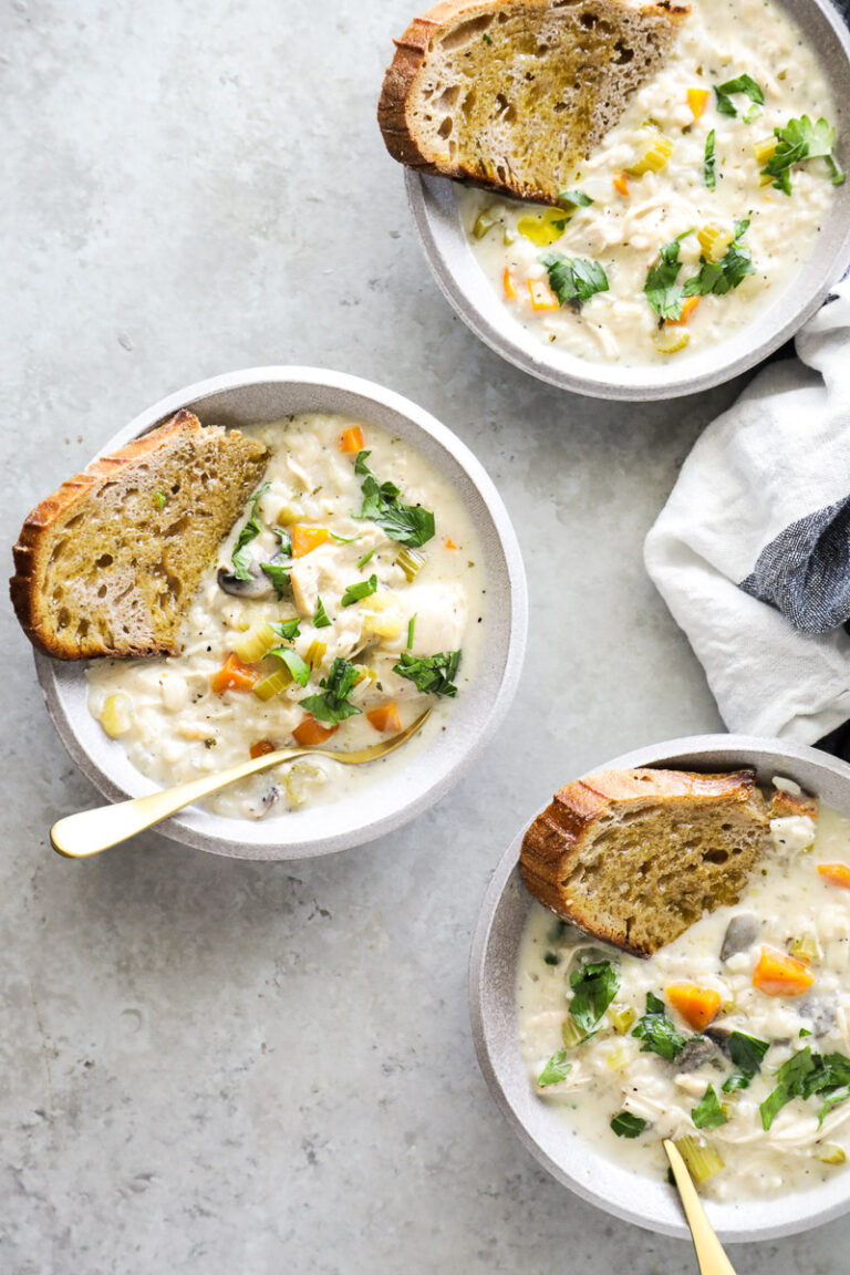 Three bowls of chicken and rice soup with a slice of bread in each soup.