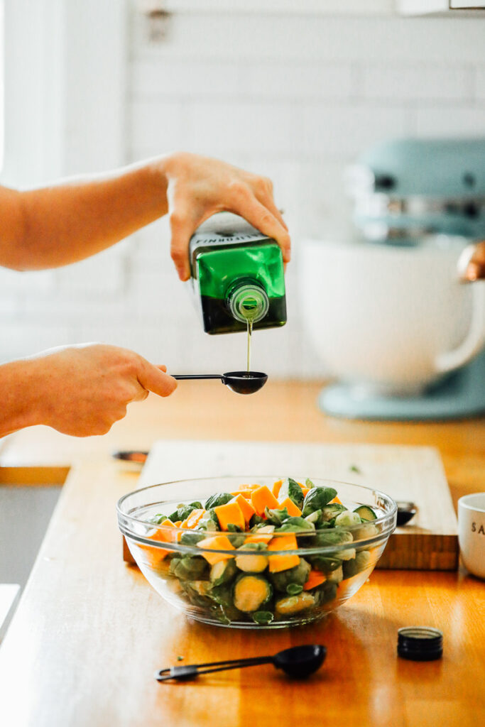 Pouring olive oil over brussels sprouts and butternut squash. 