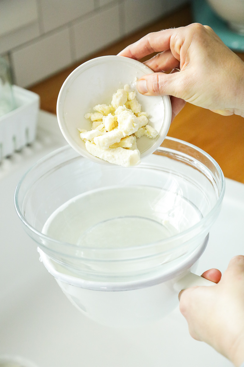 Adding shea butter to the glass bowl on top of a saucepan (double boiler).