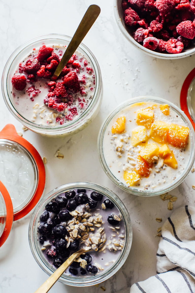 Overnight oats in three jars with frozen fruit on top: mango, blueberries, and raspberries.