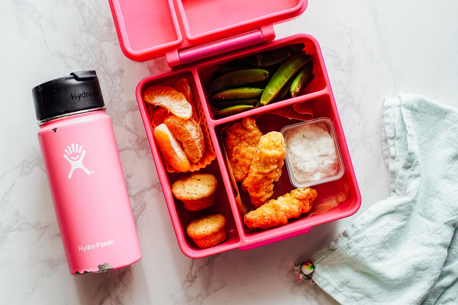 Lunchbox meal: chicken nuggets, mini muffin, orange slices, ranch dip, and sugar snap peas.