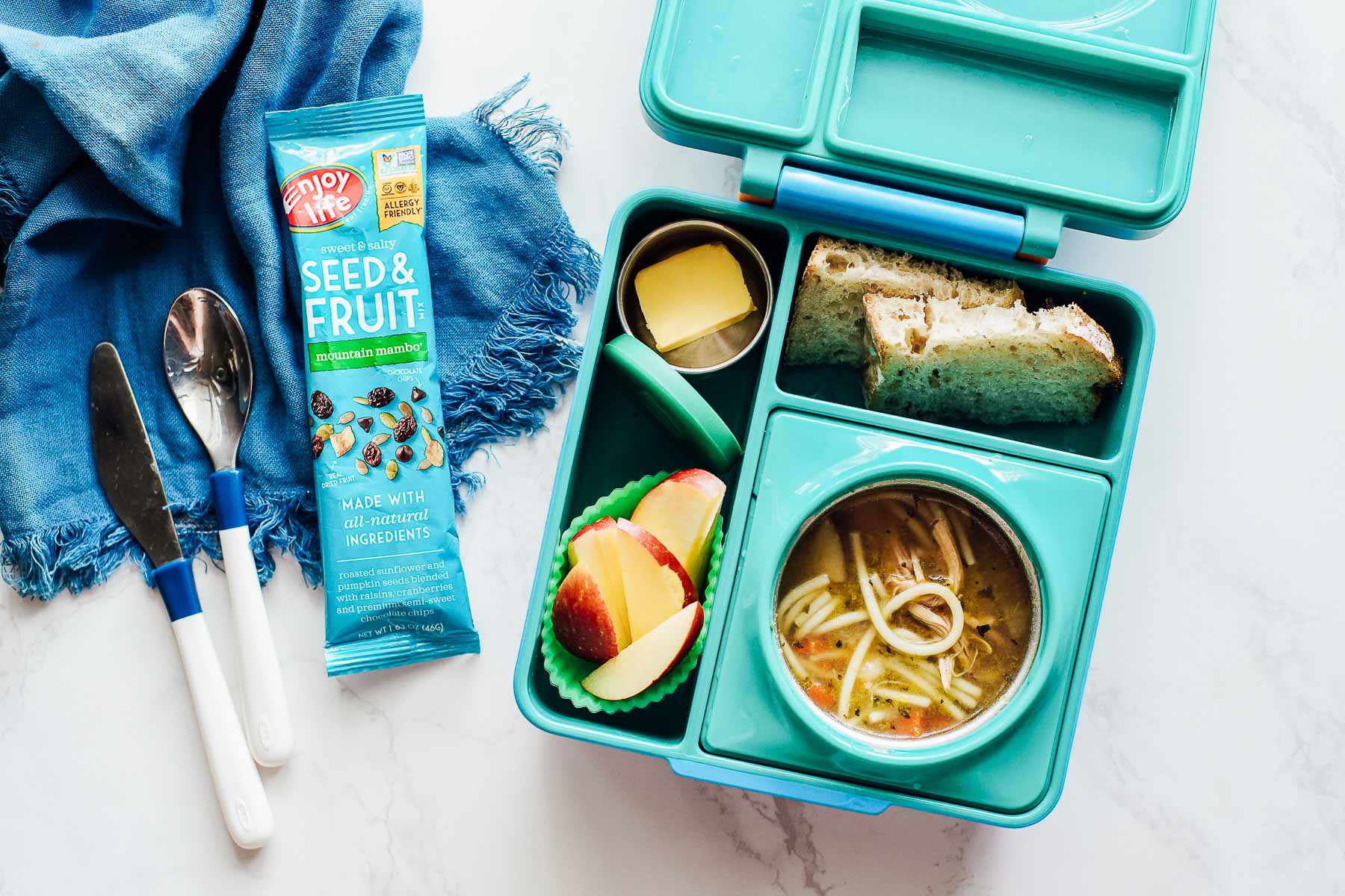 Chicken noodle soup in the lunchbox with apple slices, butter, and bread slices.