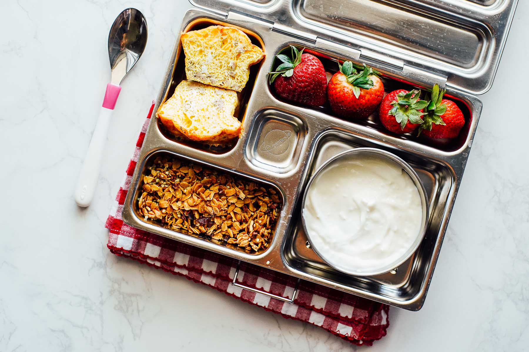 Egg omelet cup split in half, granola, yogurt, and strawberries in a bento box.