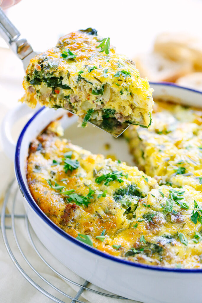 Cutting a slice of sausage and egg casserole from a baking dish.