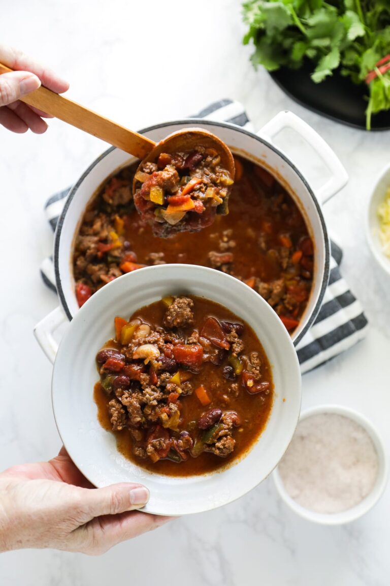 Stovetop chili being spooned into a bowl from a dutch oven.