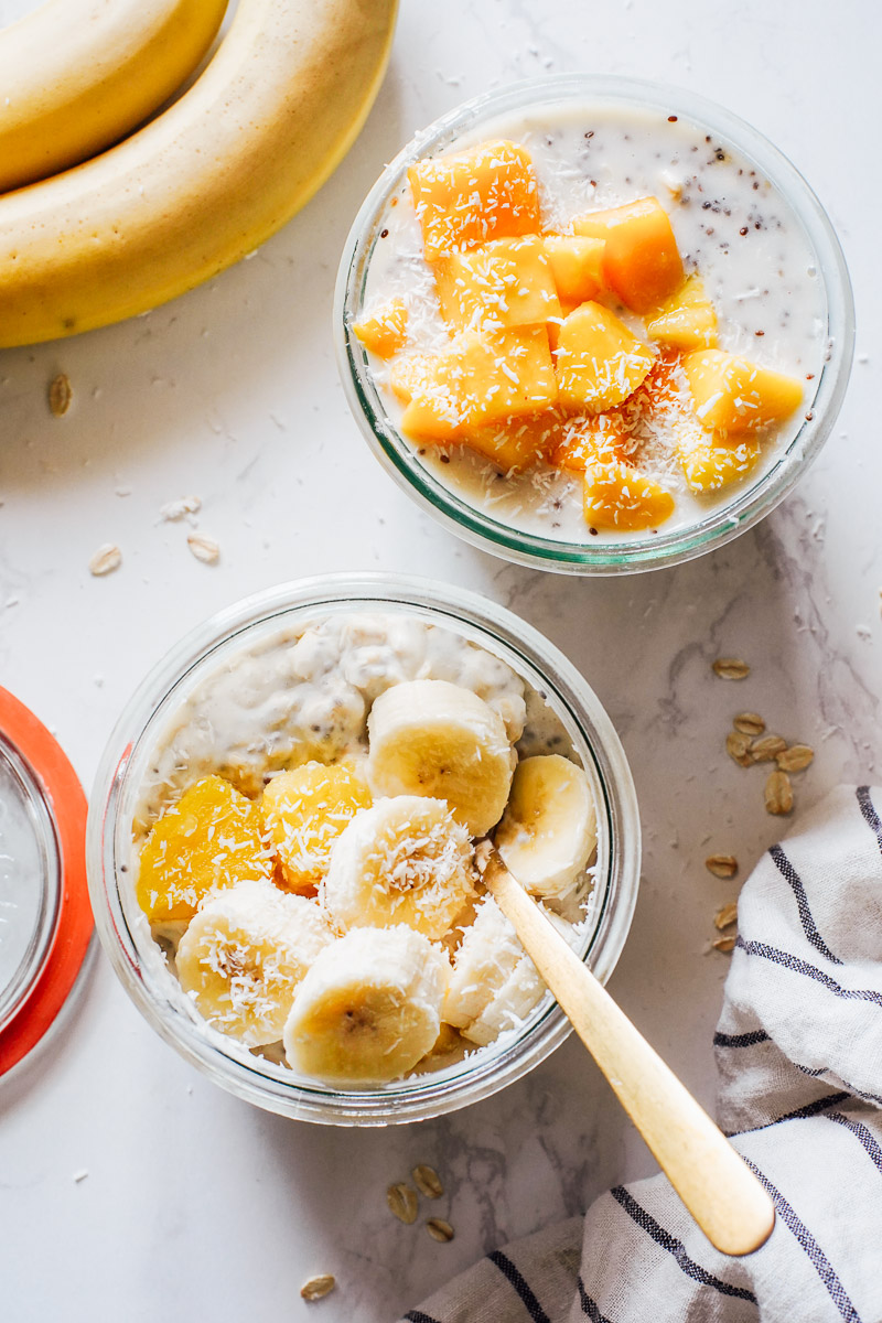 Overnight oats in glass jars topped with mango, pineapple, and banana.