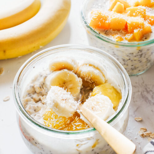 Overnight oats in glass jars topped with mango, pineapple, and banana.